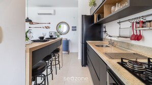 A modern kitchen with a central island, black appliances, and a hanging pot rack. - CDN - Apartments in Campeche (Florianópolis)