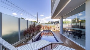 A modern outdoor pool area with a glass enclosure, wooden deck, and lounge chairs. - CDN - Apartments in Campeche (Florianópolis)