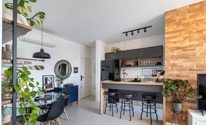 Cozinha moderna com ilha central, banquetas de bar e área de jantar com mesa de vidro e cadeiras.