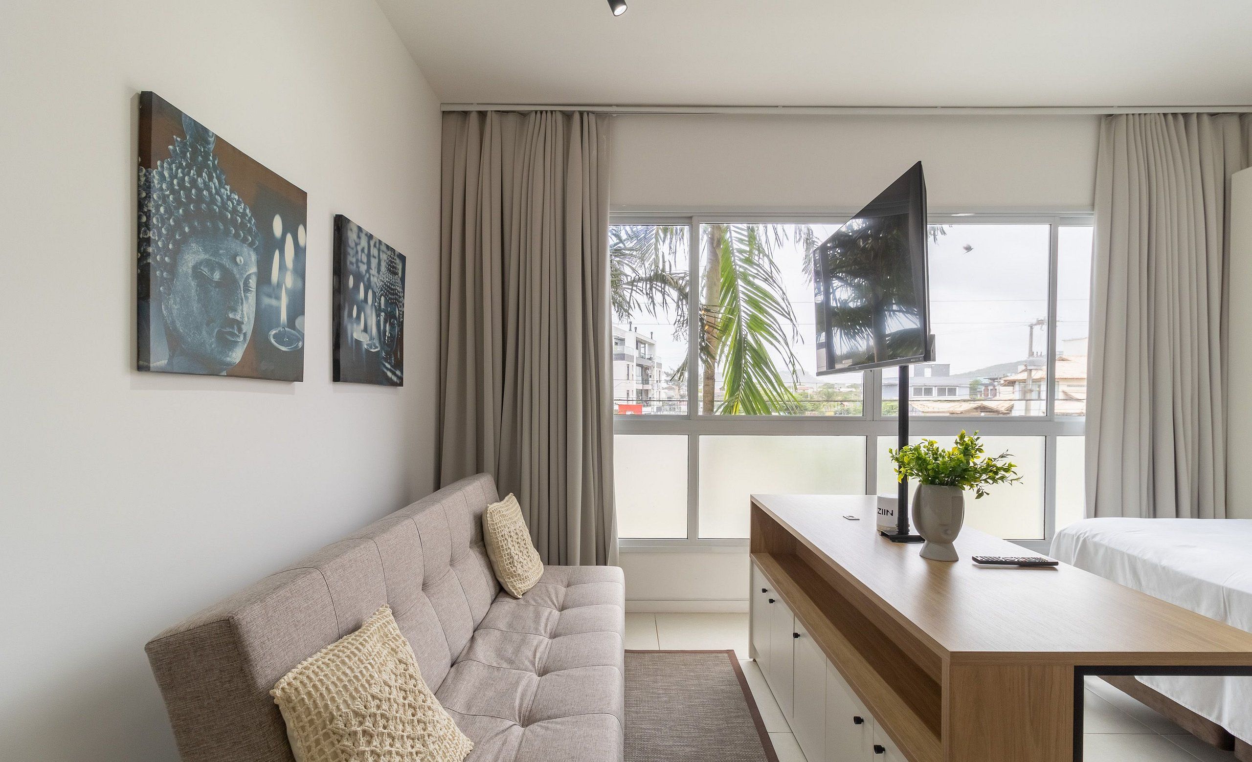 Une chambre moderne avec un canapé, une télévision, une table de chevet agrémentée d’une plante et des œuvres d’art accrochées au mur.