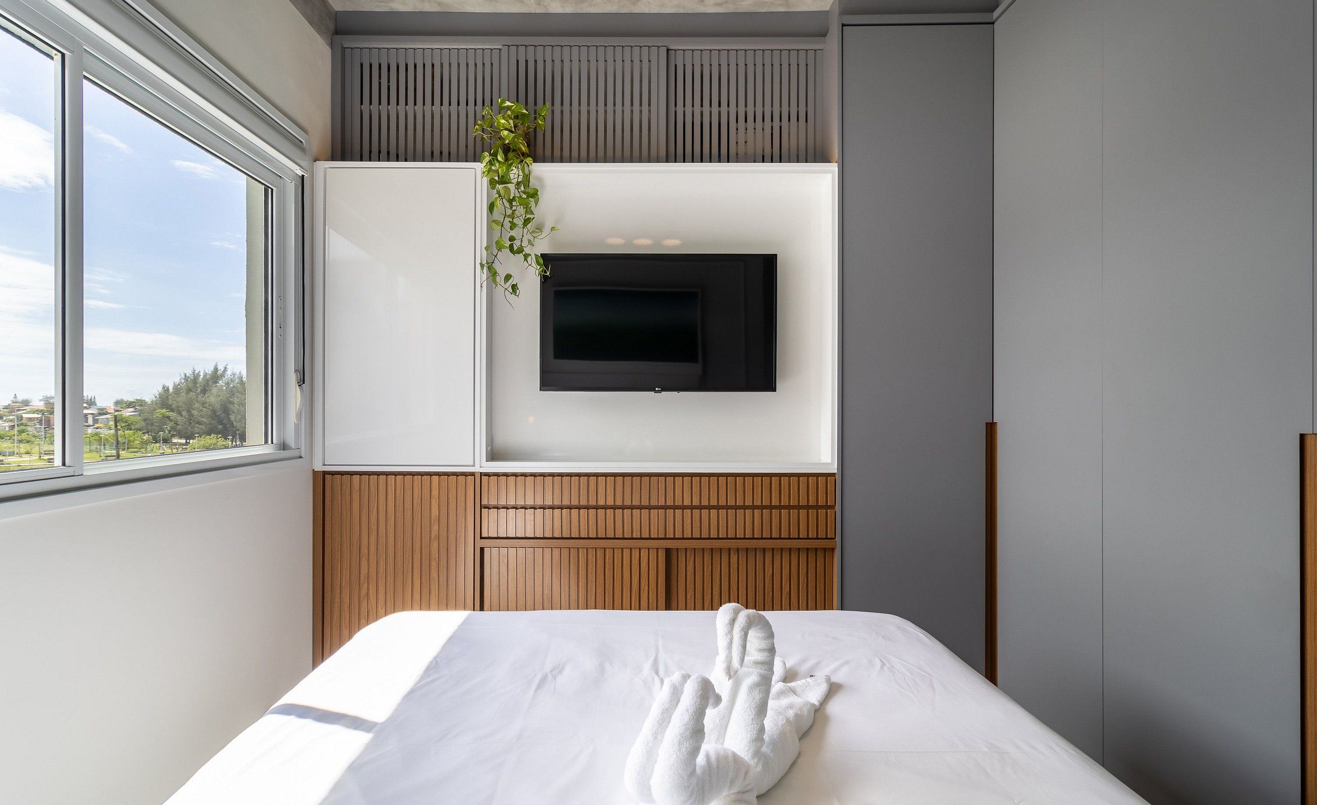A modern hotel room with a large bed, a mounted TV, and a view of the city through the window.