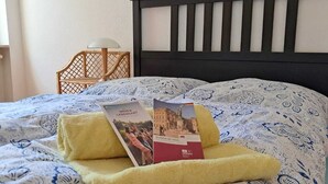 Een bed met een beddegoed met patroon, een opgevouwen handdoek en twee brochures erop.