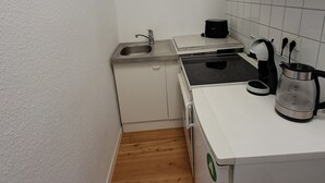 Een kleine keuken met witte kastjes, een roestvrijstalen spoelbak, een zwarte elektrische waterkoker en een koffiezetapparaat op het aanrecht.