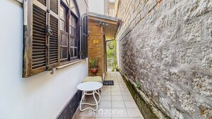 Une ruelle étroite avec un mur blanc, une porte en bois et une petite table accompagnée d’une chaise.