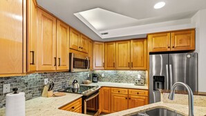 A modern kitchen with wooden cabinets, stainless steel appliances, a granite countertop, and a skylight.