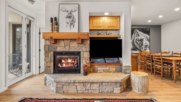 A modern living room with a stone fireplace, wooden cabinets, and a dining area with a wooden table and chairs.