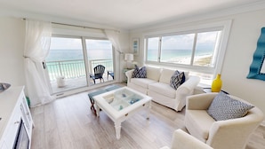 A spacious living room with a white sofa, a glass coffee table, and a view of the beach through large windows. - Destin Towers 113 2 Bedroom Condo (Destin)