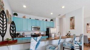 Une cuisine moderne avec des armoires de couleur turquoise, un îlot central et des sièges de type bar, agrémentés de chaises à motifs de feuilles.