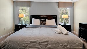 Ein Schlafzimmer mit einem großen Bett, zwei Nachttischen, einem Kopfteil und zwei Fenstern mit Jalousien.