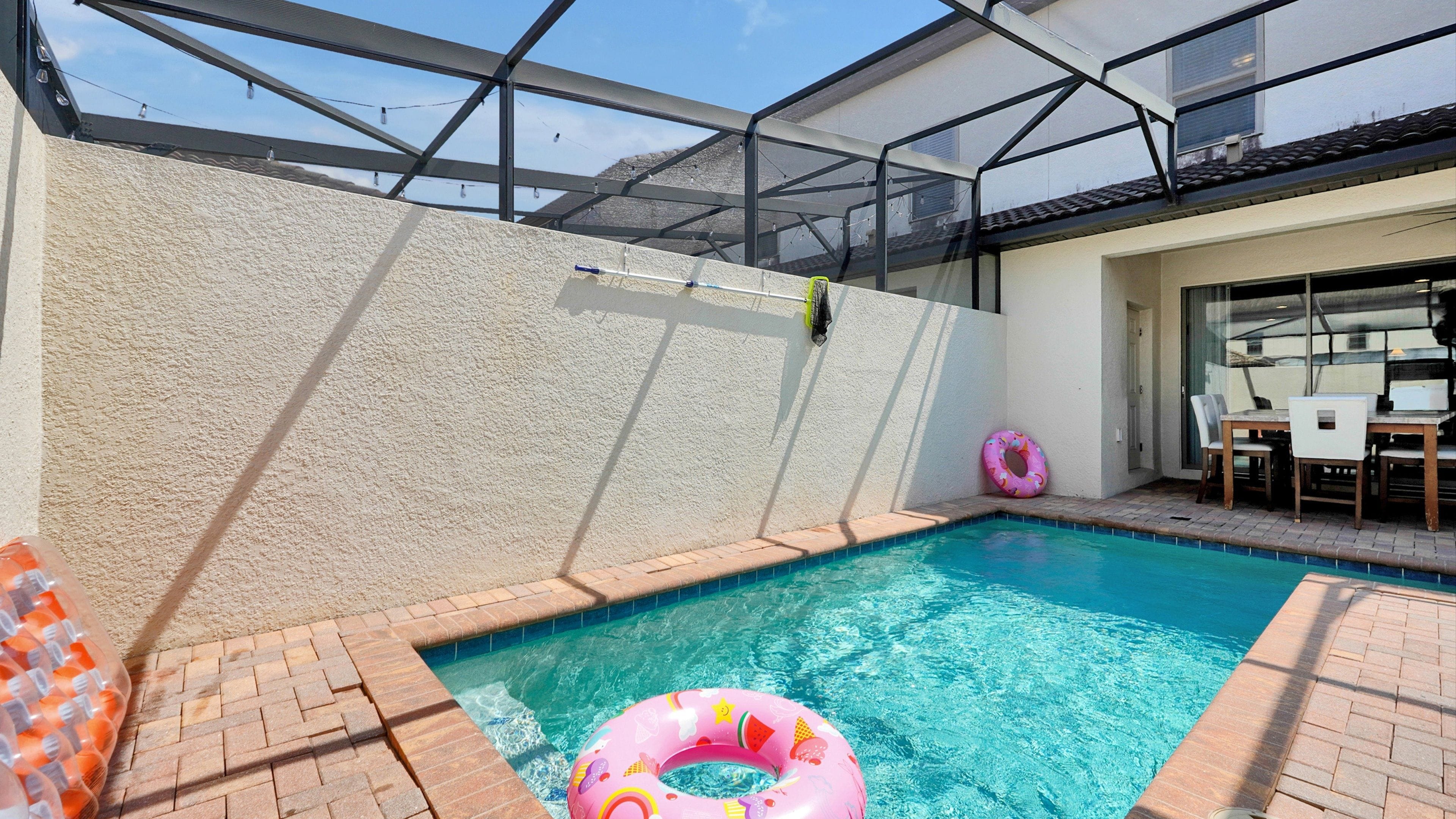 Una piscina con techo de vidrio, borde de ladrillo y una mesa con sillas.