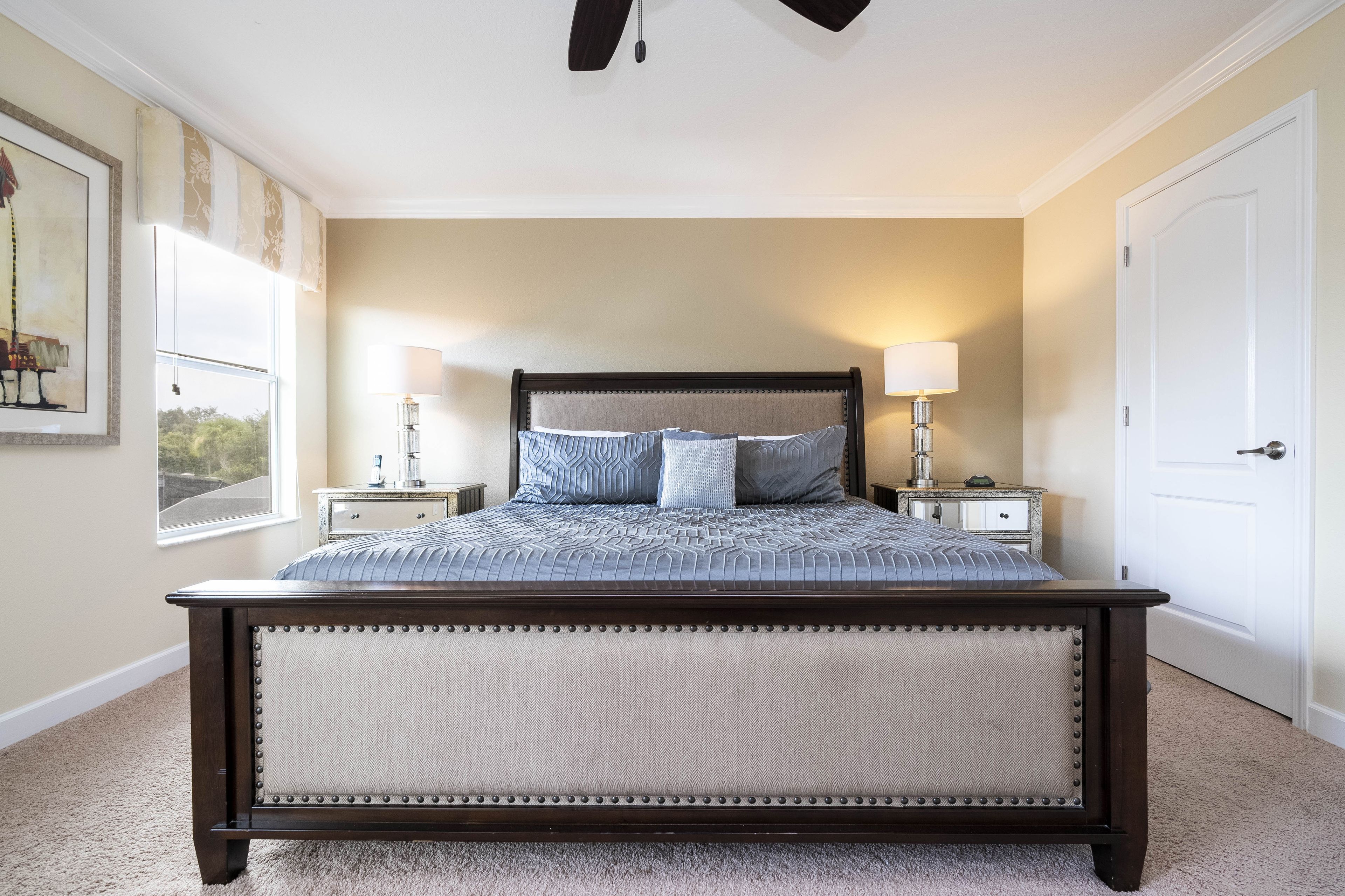 A bedroom with a large bed, two bedside tables, a nightstand, a door, and a window.