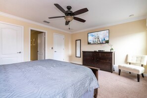Un dormitorio con cama, ventilador de techo, cómoda, silla y televisor en la pared.