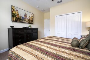 A bedroom with a large bed, a dresser, a wall-mounted TV, and a door. - Family Pool Home Near Disney!! Modern Decor, Bbq ,resort W/ Tons Of Amenities! 6 Bedroom Home (Kissimmee)