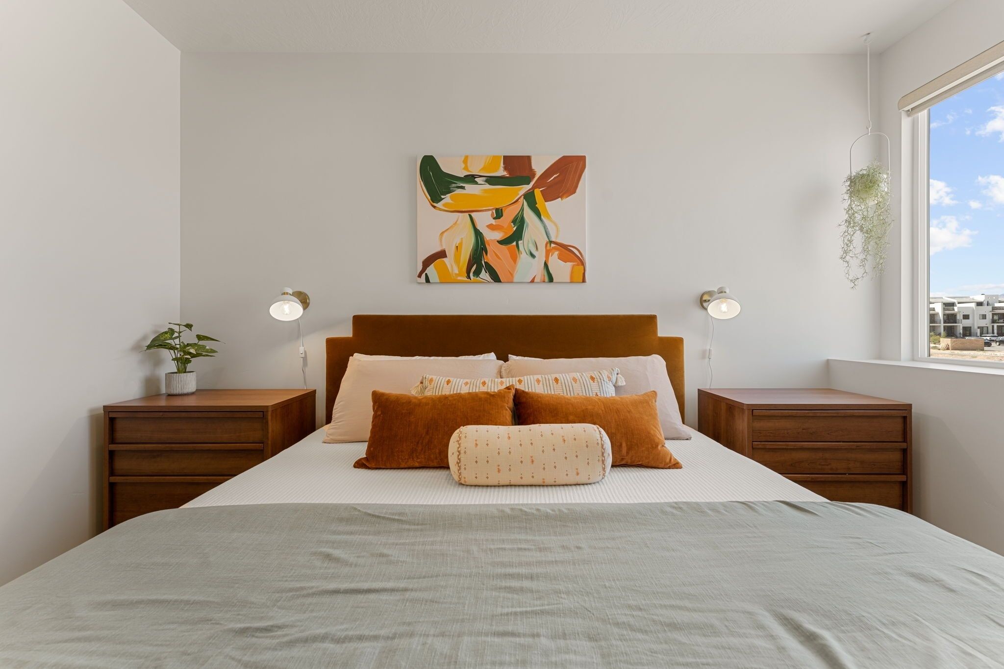 Un dormitorio moderno con una cama grande, dos mesitas de noche, un cuadro colgado en la pared y una ventana con vistas.