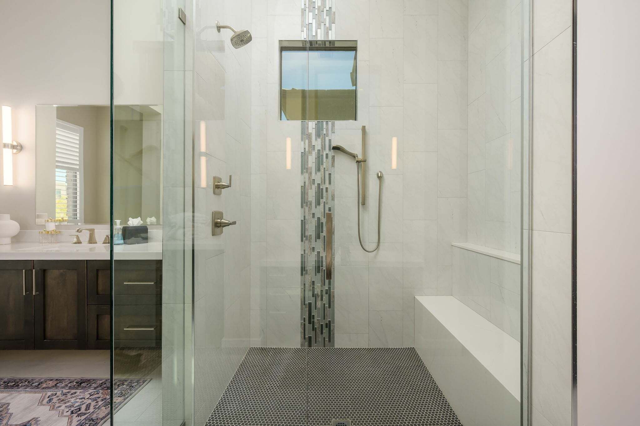 A modern bathroom with a glass-enclosed shower, a vanity with a mirror, and a patterned floor.