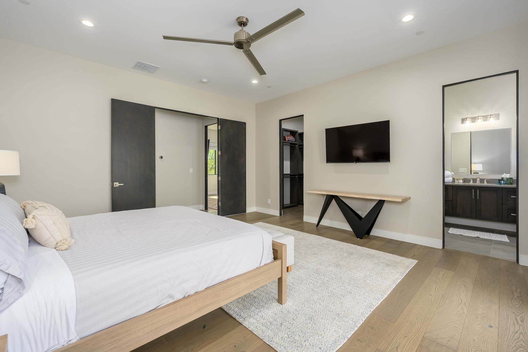 A modern bedroom with a bed, a ceiling fan, a TV, and a mirror.