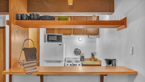 Uma cozinha compacta com bancada de madeira, micro-ondas embutido, fogão e um escorredor de louça suspenso.