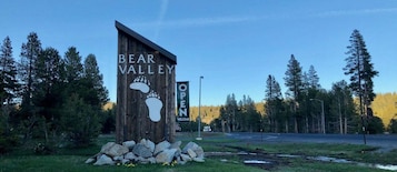 Un letrero de madera que dice "BEAR VALLEY OPEN" y un símbolo de huella de pata.
