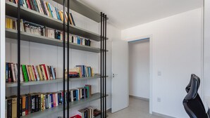 Una habitación moderna con una amplia estantería llena de libros, una silla negra y una puerta blanca al fondo.