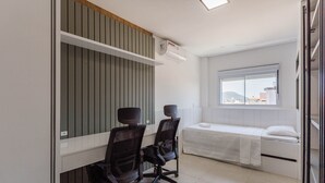 Un dormitorio moderno con cama, escritorio y dos sillas, y una ventana con vista a la ciudad.