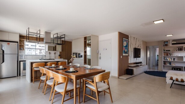 Una cocina moderna con electrodomésticos integrados, un comedor con sillas de madera y una sala de estar con sofá y televisor.
