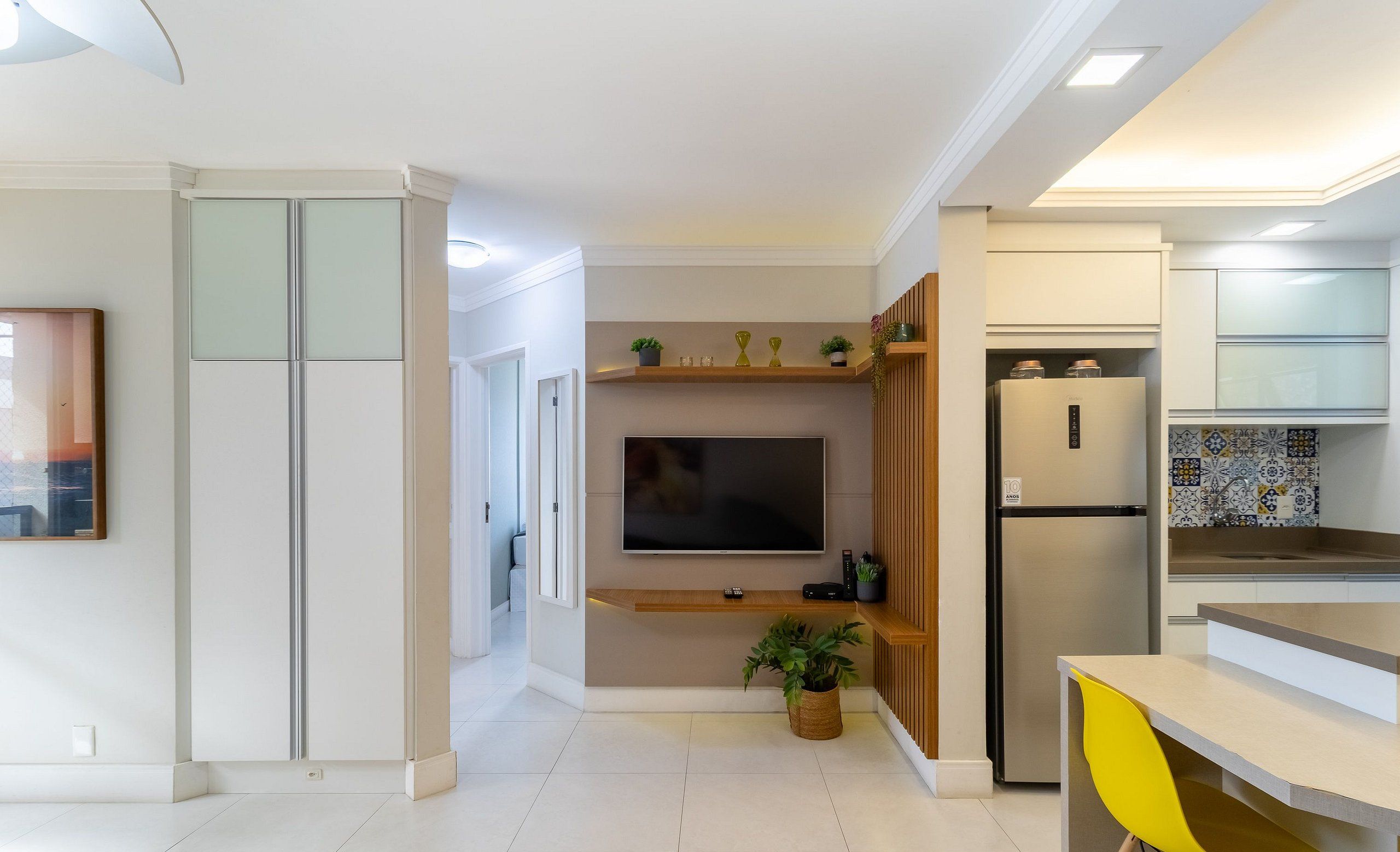 Una cocina moderna con televisor integrado, refrigerador y zona de comedor con una silla amarilla.