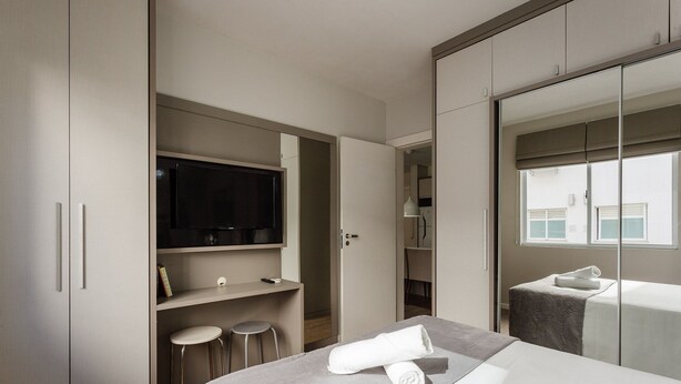 A modern hotel room with a bed, a TV, a desk, and a seating area.