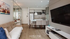 A modern living room with a sofa, a TV, and a kitchen area with a dining table and chairs.