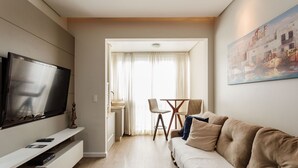 A modern living room with a flat-screen TV, a sofa, and a dining area with a table and chairs.