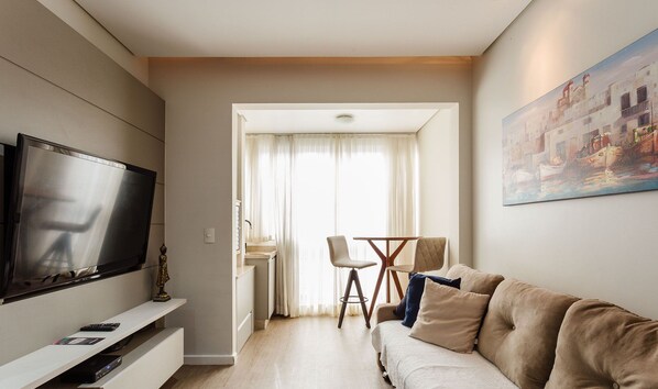 Una sala de estar moderna con un televisor de pantalla plana, un sofá y una zona de comedor con una mesa y sillas.
