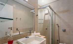 Un baño moderno con ducha de vidrio, un espejo grande y un lavabo con dispensador de jabón.