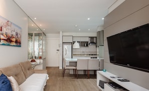 Un salon moderne comprenant un canapé, un téléviseur et un coin cuisine avec une table à manger et des chaises.