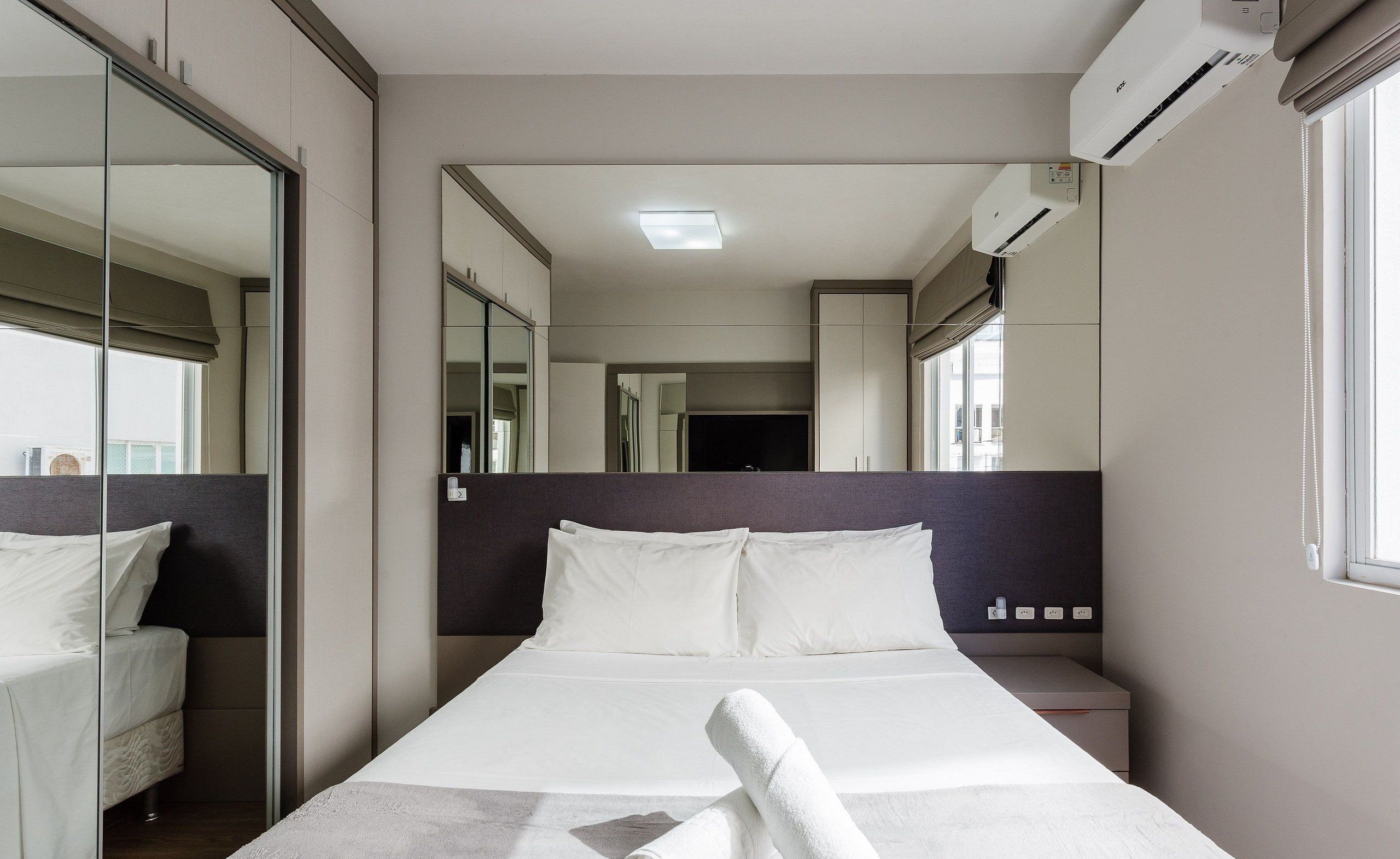 A modern hotel room with a large bed, a bedside table, a nightstand, a mirror, and an air conditioning unit.
