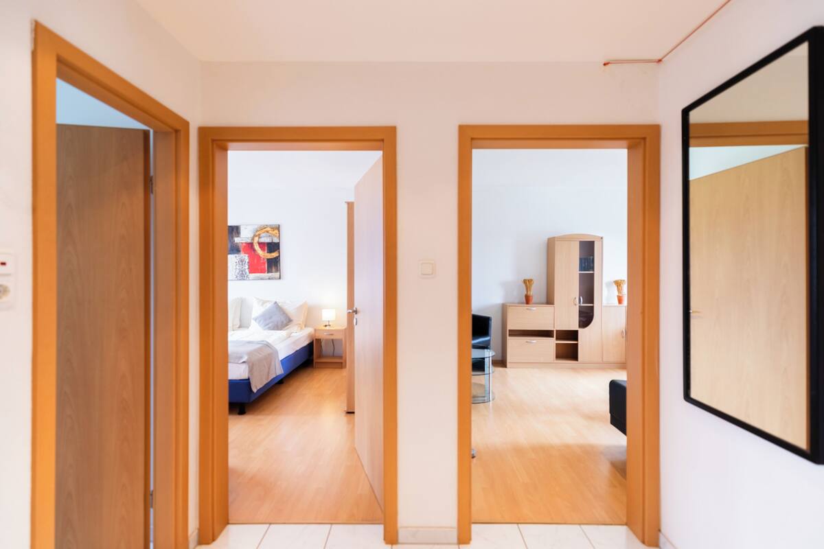 A hallway leading to a bedroom with a bed, bedside table, and a wardrobe.