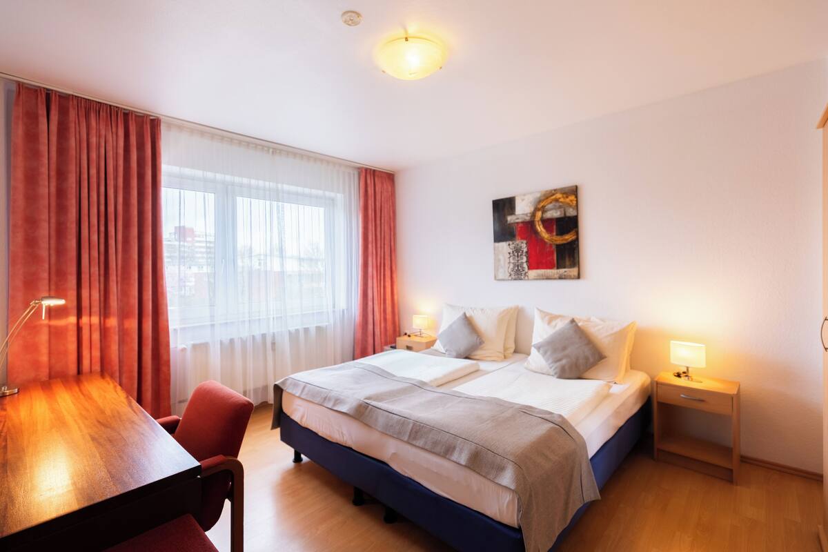 A hotel room with a bed, bedside tables, a desk, and a chair.