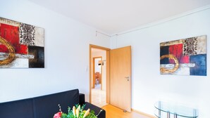 A modern living room with a black sofa, a glass coffee table, and two abstract paintings on the walls. - acora Bremen Garden Living the City (Bremen)