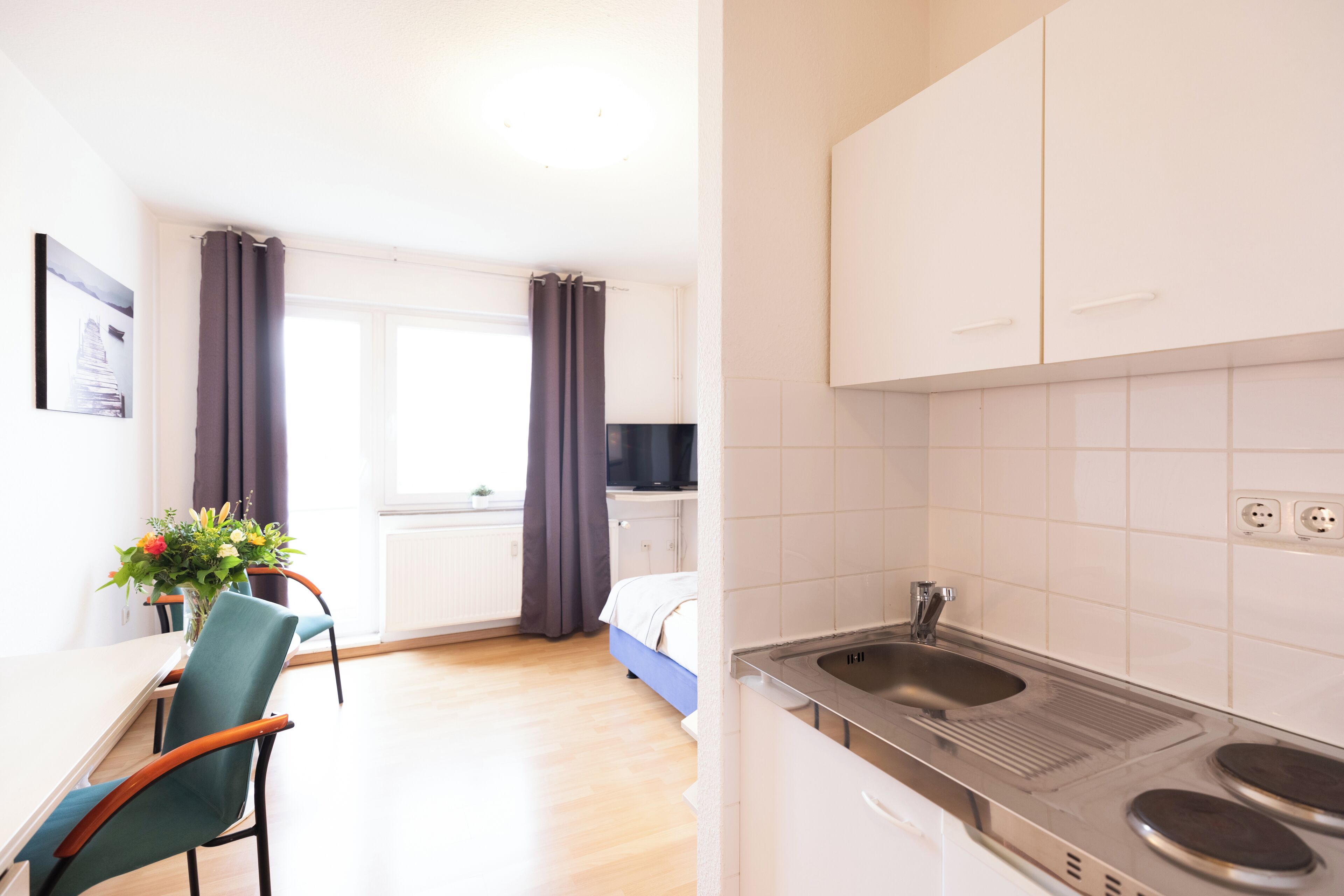 A modern kitchen with white cabinets, a double sink, and a dining area with a table and chairs.