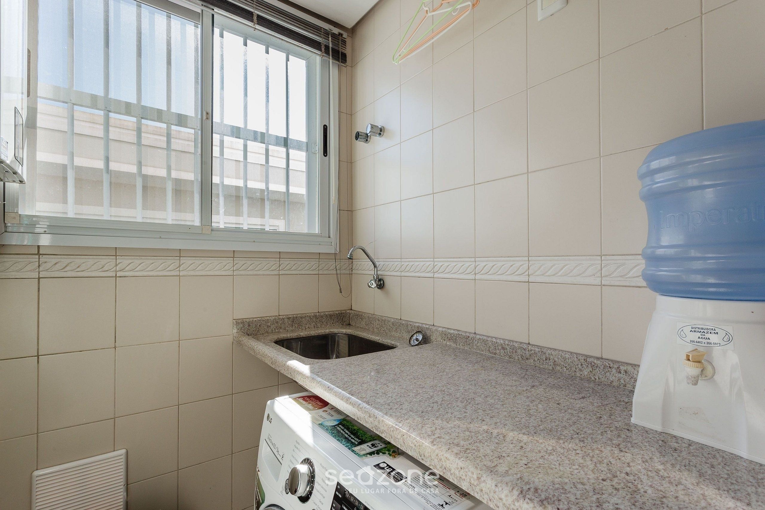 A kitchen with a granite countertop, a sink, a window with blinds, and a water dispenser.