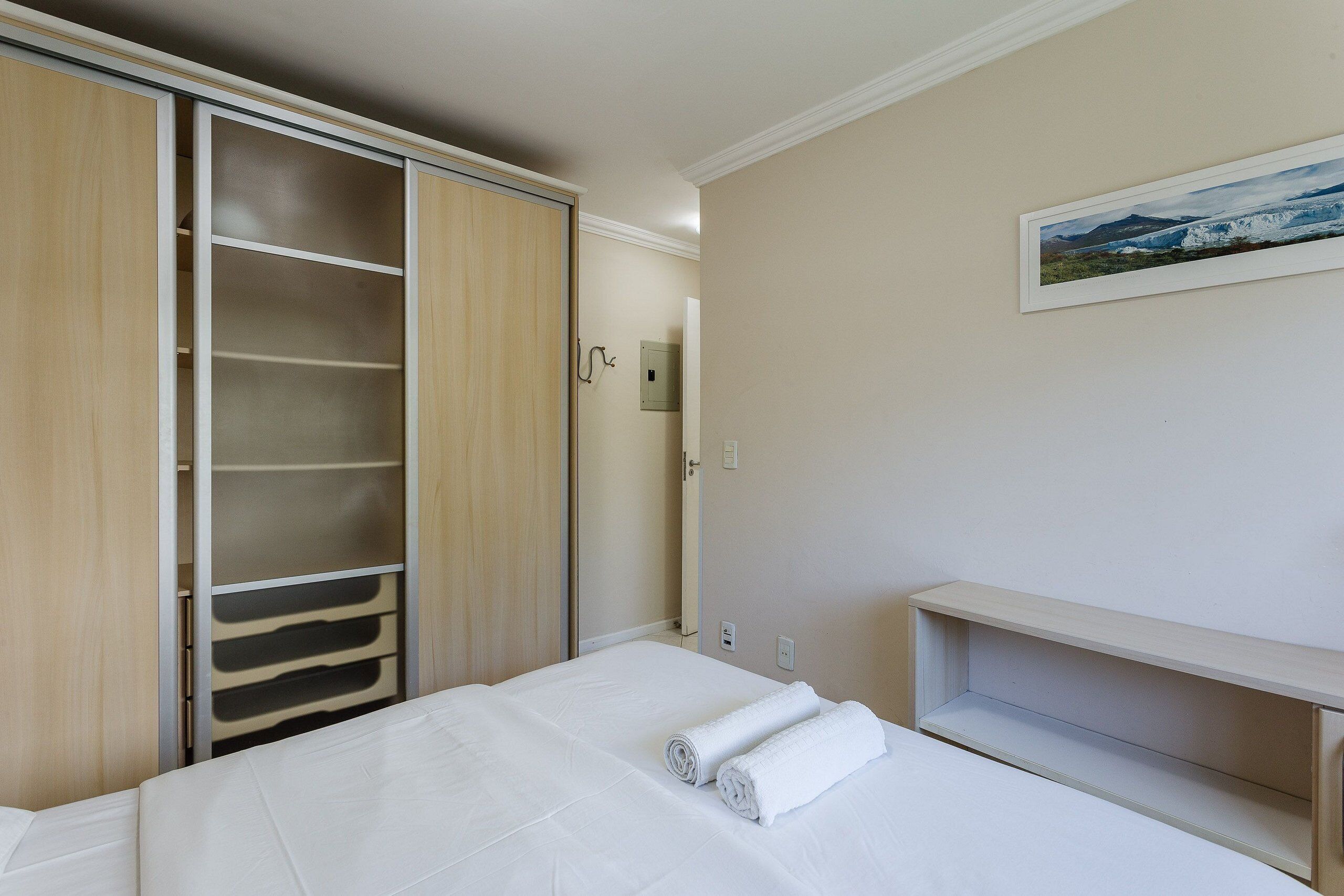 A hotel room with a bed, a wardrobe, a shelf, and a painting on the wall.