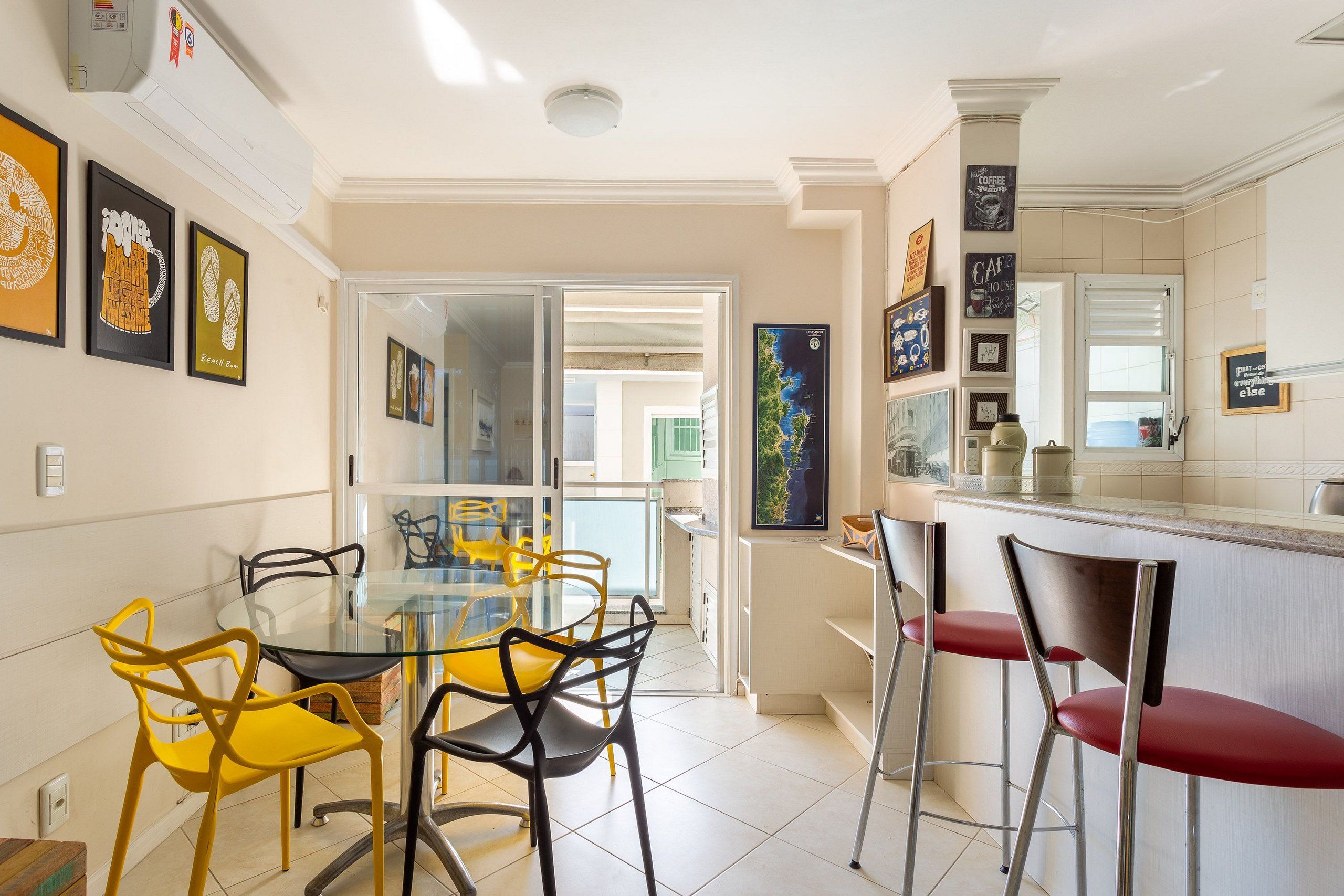 A modern kitchen with a glass dining table and colorful chairs, a bar area with stools, and a view of the outside.