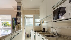 A modern kitchen with white cabinets, a granite countertop, a built-in microwave, and a stainless steel sink. - Apto espaçoso com piscina 750m da praia | CHR025 (Florianópolis)