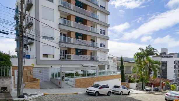 Un edificio de varios pisos con balcones, un estacionamiento con automóviles y un letrero que dice 'STUDIO VENUTO'.