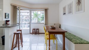 A modern kitchen with a dining area, a bench, and a window with a view of buildings and palm trees.