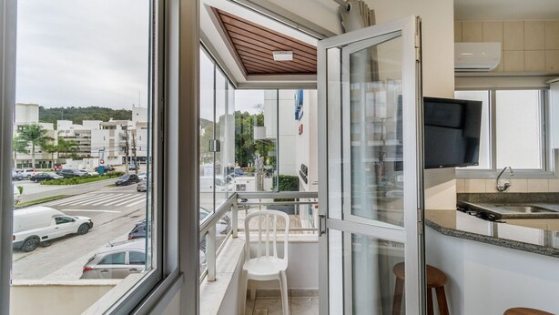 A balcony with a view of a street and buildings, a white chair, and a kitchen area with a TV and sink.