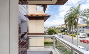 A balcony with a view of a street, palm trees, and buildings. - Fully Equipped Apartments Just Minutes From Jurere Beach - CIE (Florianópolis)