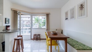 Une cuisine moderne avec un coin repas, un banc et une fenêtre donnant sur des immeubles et des palmiers.
