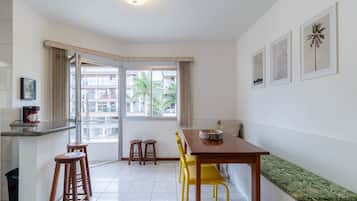 A modern kitchen with a dining area, a bench, and a window with a view of buildings and palm trees.