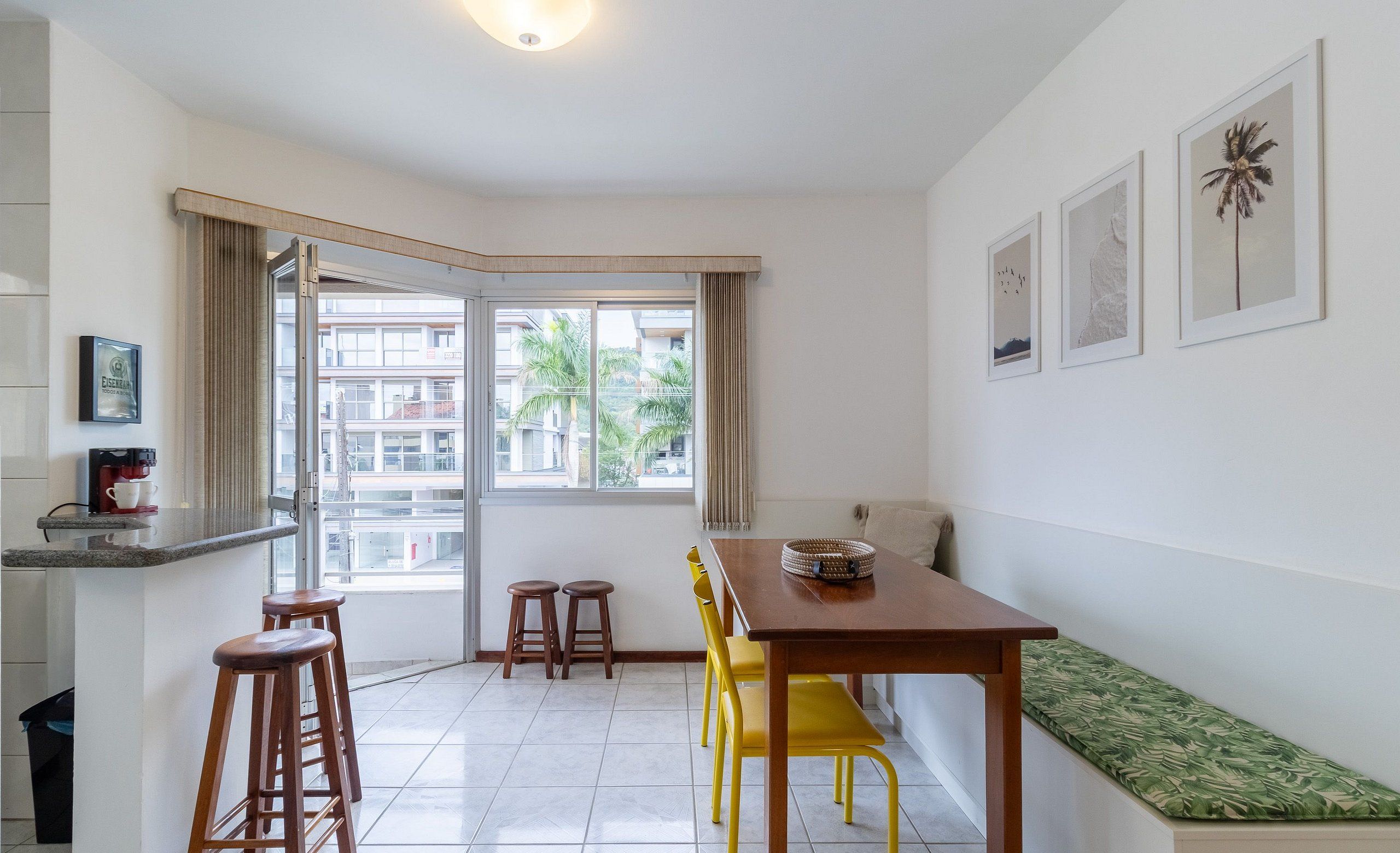 A modern kitchen with a dining area, a bench, and a window with a view of buildings and palm trees.