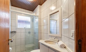 A bathroom with a glass shower enclosure, a toilet, a sink with a mirror, and a towel on the counter. - Fully Equipped Apartments Just Minutes From Jurere Beach - CIE (Florianópolis)