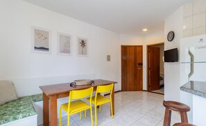 A dining area with a wooden table, yellow chairs, and a bench. There are framed pictures on the wall and a television mounted above the table. - Fully Equipped Apartments Just Minutes From Jurere Beach - CIE (Florianópolis)